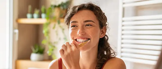 Richtig Zähne putzen: Junge Frau putzt ihre Zähne vorm Spiegel